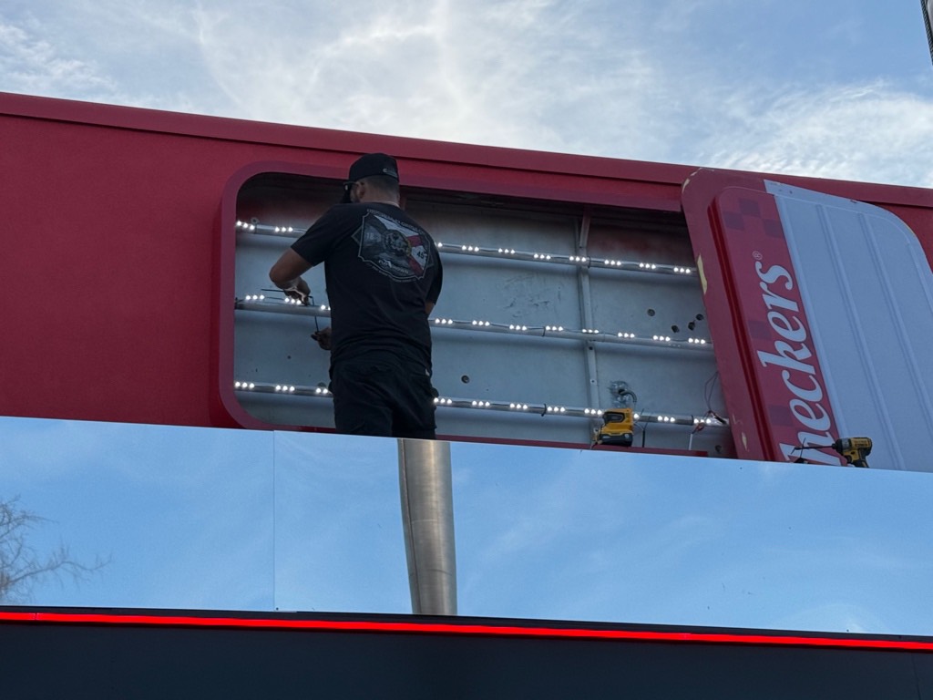 Sign installer working inside illuminated monument sign during professional installation