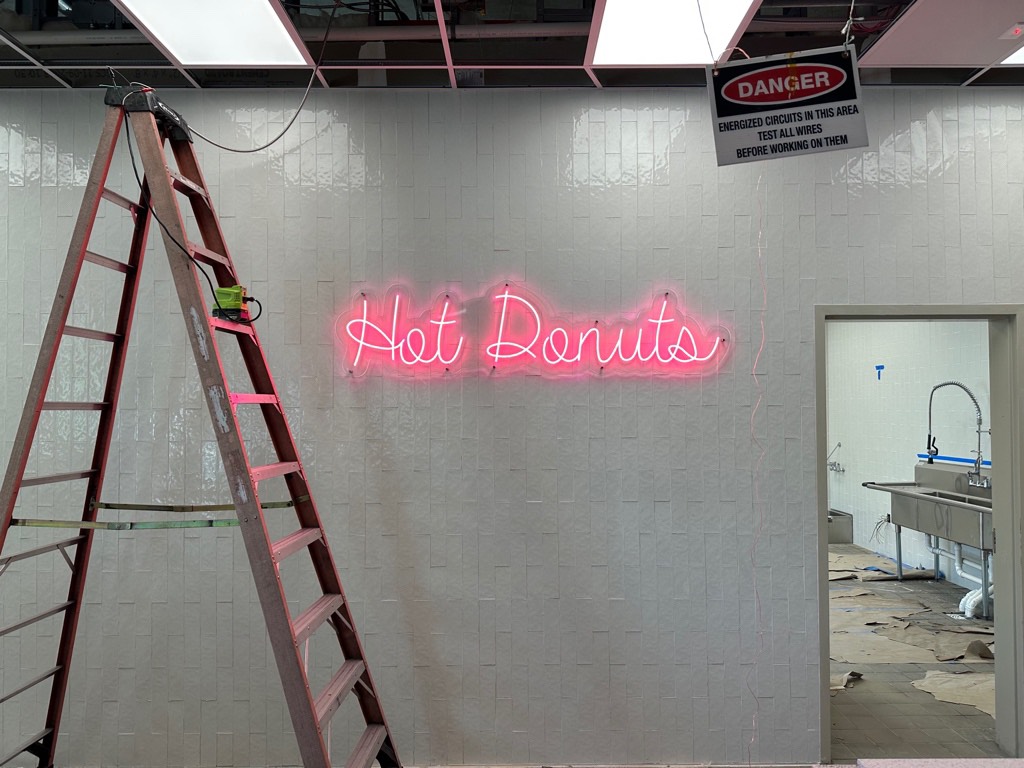 LED neon-style sign being installed on interior wall with ladder