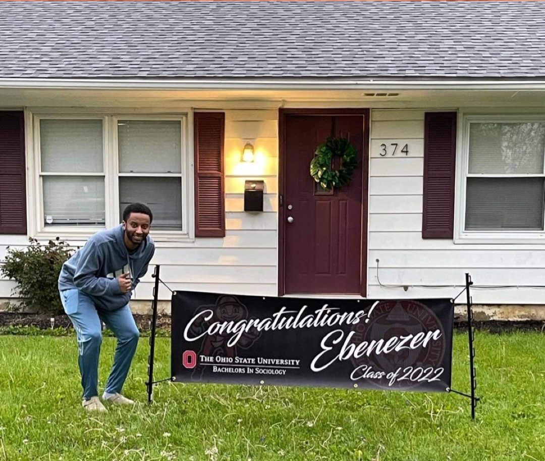 Graduate standing beside a personalized graduation banner, representing the transition from graduation day to future milestones