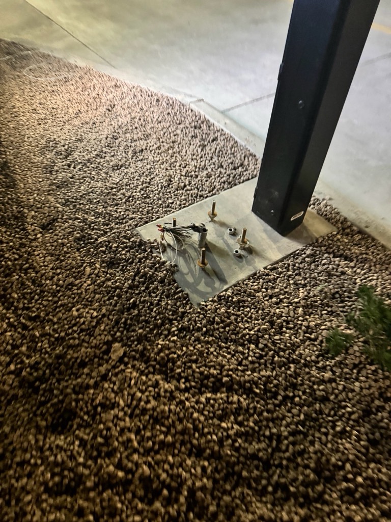 Steel base plate with anchor bolts and electrical wiring for commercial sign installation.