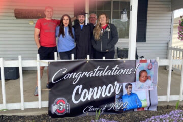 Family celebrating a high school graduation on a front porch with a personalized graduation banner displayed on the railing